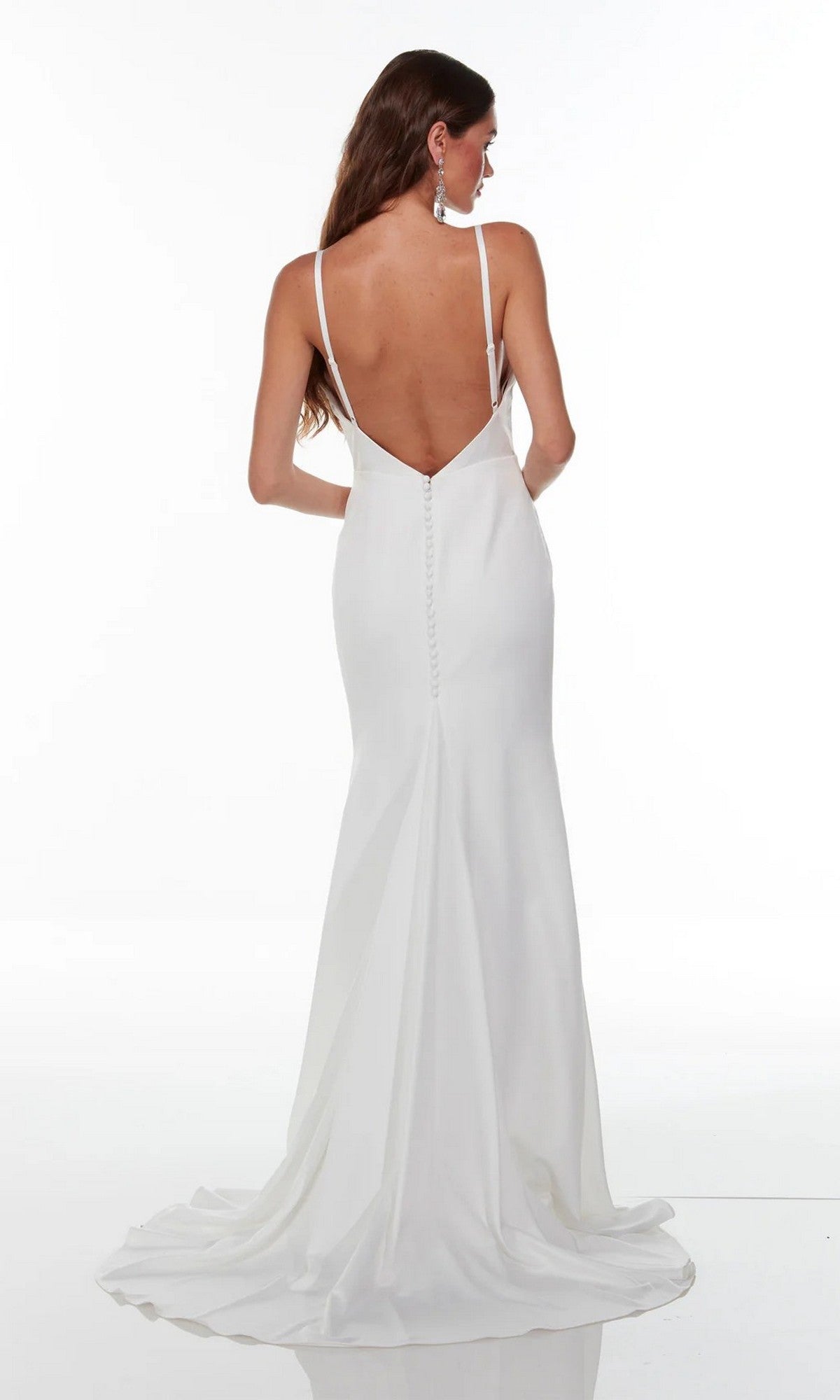 A woman wearing the Alyce 7051 long white dress—a modern bridal gown with a cowl neckline, deep V-back, thin straps, button details, and a small train—stands against a plain white background.